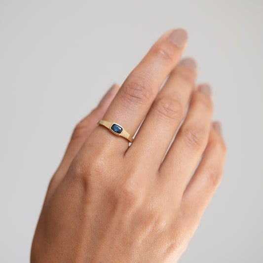 Gold ring with a blue stone on a hand against a plain background