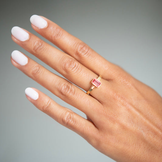 Hand wearing a pink gemstone ring on a gray background