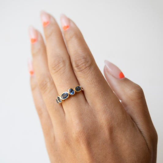 Hand wearing a gold ring with three dark gemstones on a light background