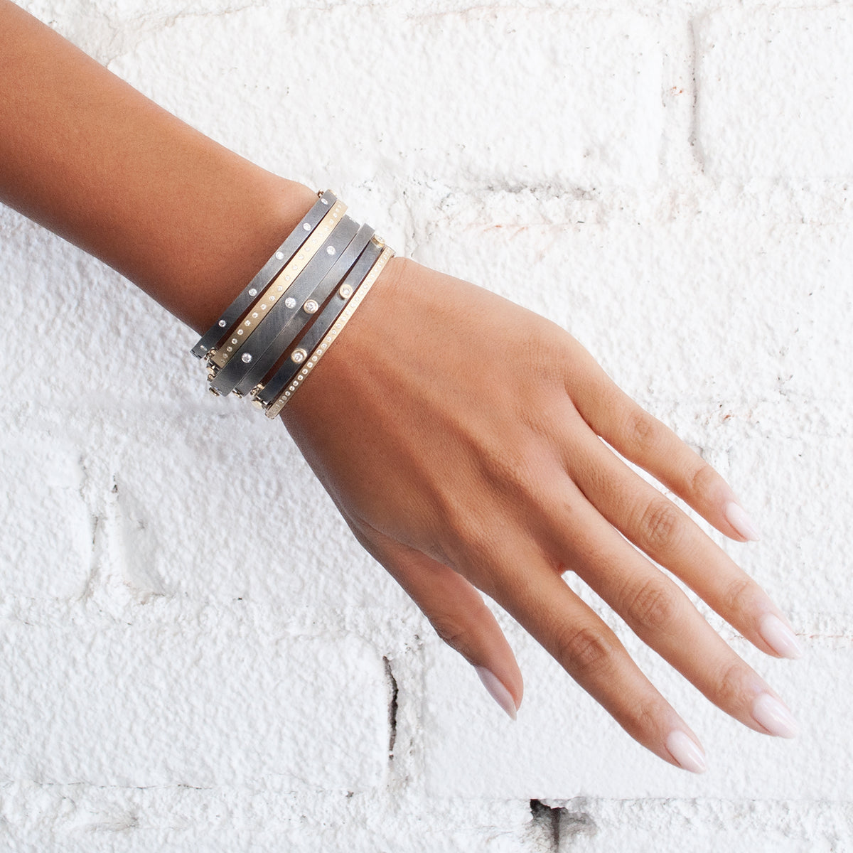 Rene Escobar - Hand wearing multiple bracelets on a textured white background