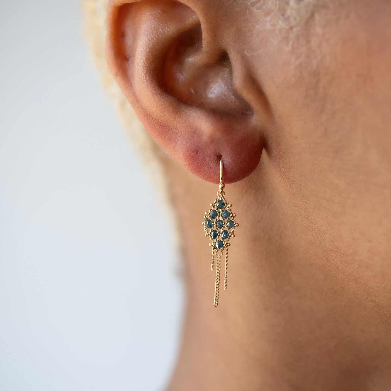 Gold earring with blue gemstones worn by a person on a plain background