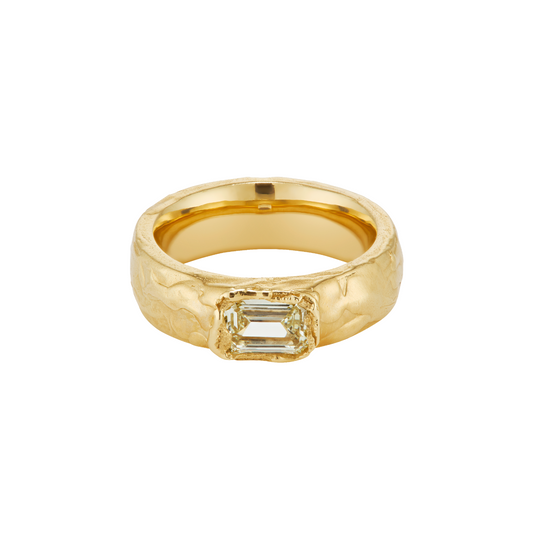 A textured yellow gold ring featuring a rectangular baguette-cut clear gemstone in a bezel setting, shown against a plain white background.