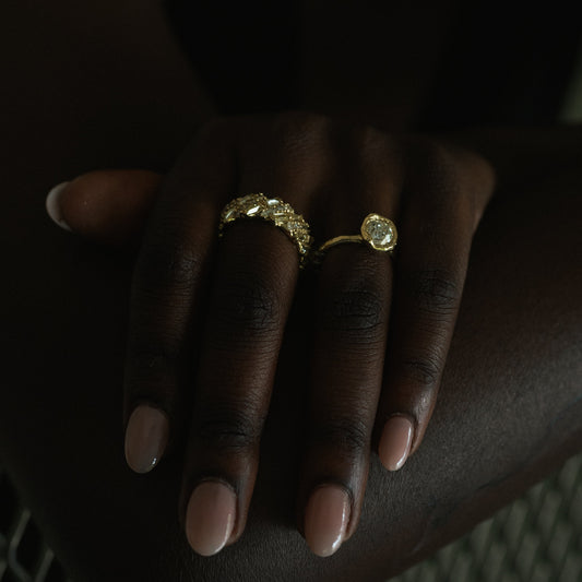 Ellis Mhairi Cameron - Hand wearing a gold ring with a large gemstone on a dark background