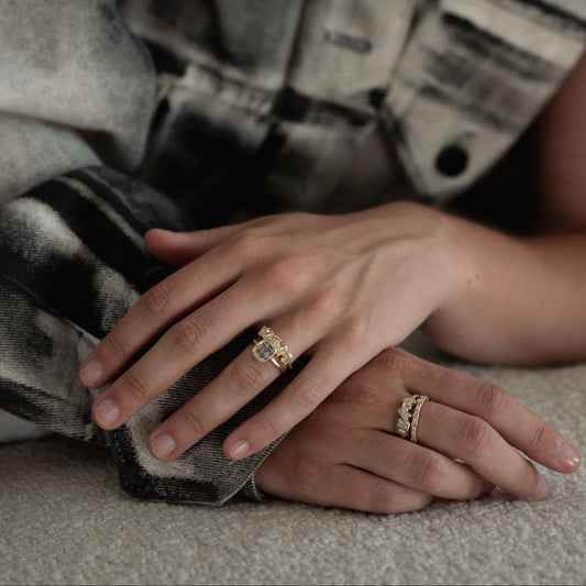 Close-up of a person's hands with gold rings, wearing a plaid shirt.