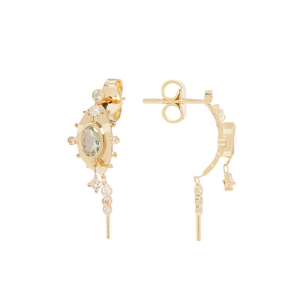 A pair of gold hoop earrings with a central oval green gemstone, surrounded by small clear stones, and featuring dangling chain elements, shown on a plain white background.