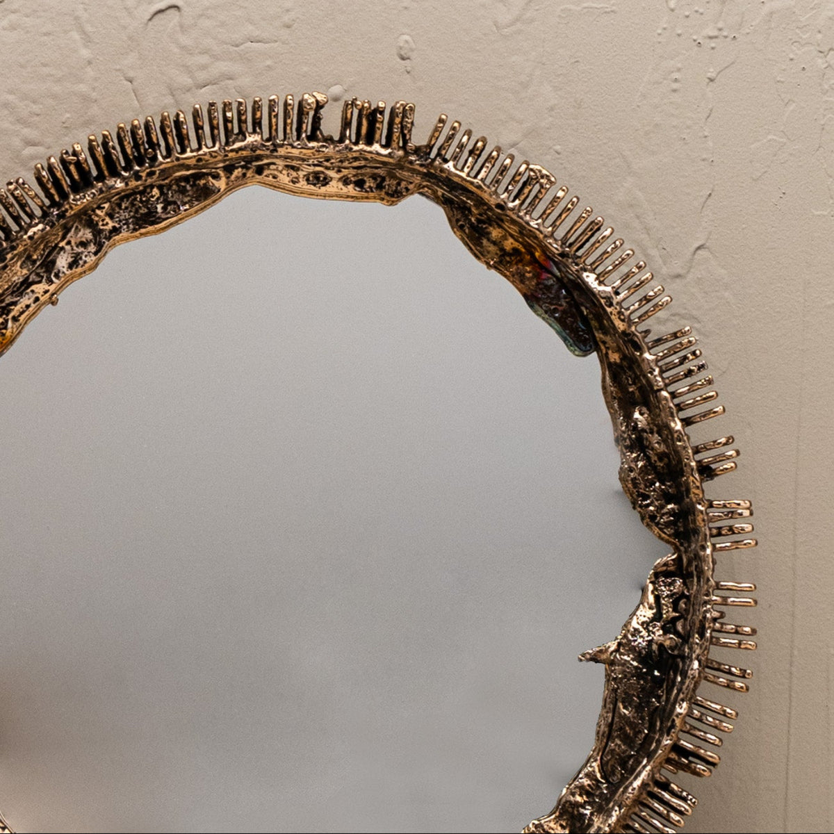 Decorative mirror with a textured bronze frame on a plain wall.