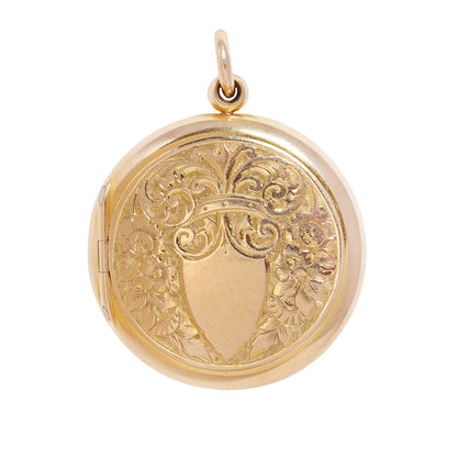 A round yellow gold locket pendant with an engraved floral pattern and a blank shield in the center, shown on a plain white background.