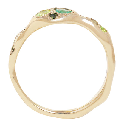 A gold ring with a wavy, organic-shaped band and small green gemstone accents along the top, shown on a plain white background.