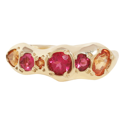A gold ring featuring a row of round and oval pink gemstones and smaller orange gemstones, set against a plain white background.