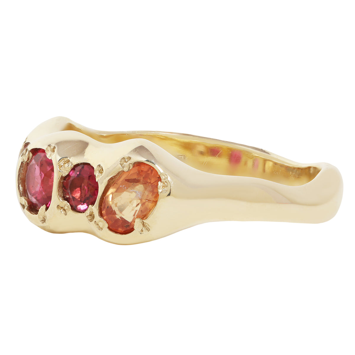 A yellow gold ring featuring three oval gemstones in pinkish-red and peachy-orange tones, set against a plain white background.
