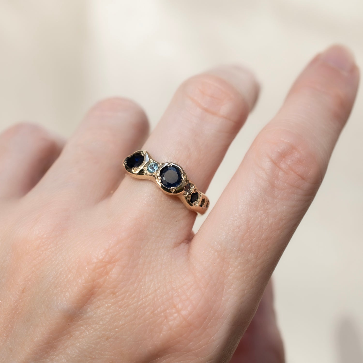 Gold ring with blue gemstones on a hand against a neutral background