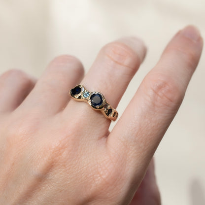 Gold ring with blue gemstones on a hand against a neutral background