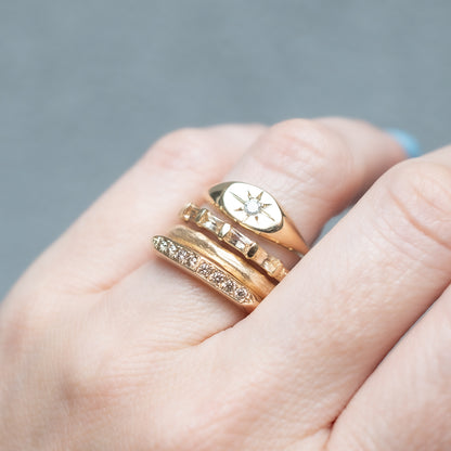 ladha - Close-up of a hand wearing three gold rings with a gray background