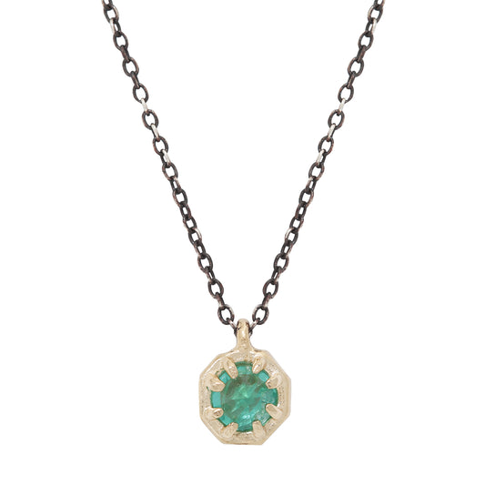 Emerald pendant set in gold on an oxidized silver chain against a white background