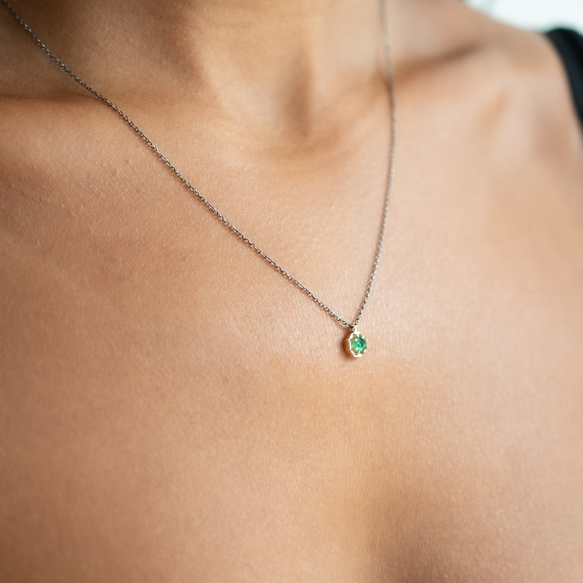 Emerald pendant set in gold on an oxidized silver chain on person