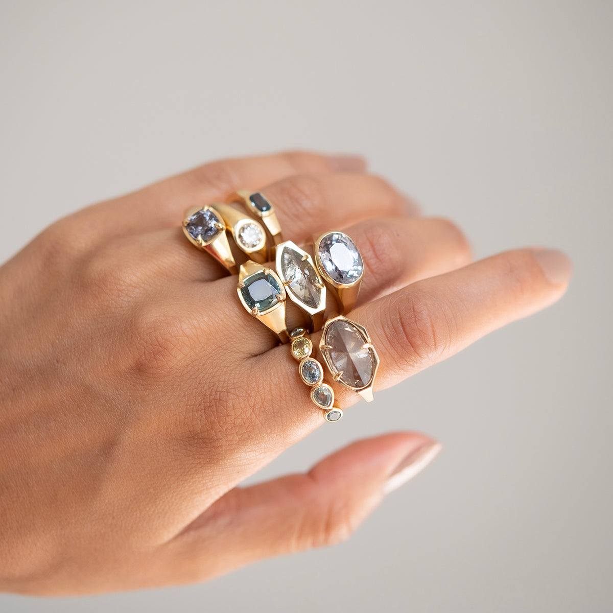 Hand wearing multiple gold rings with gemstones on a neutral background