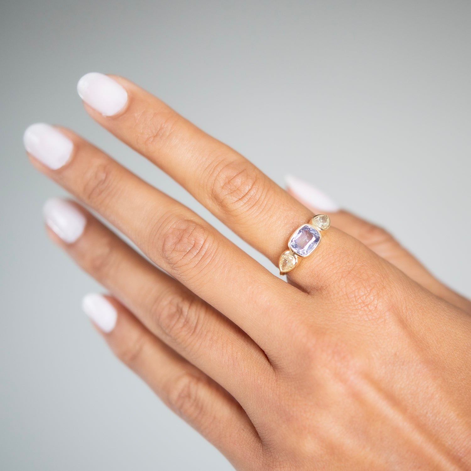 Lauren Wolf - Hand wearing a gold ring with a purple gemstone on a neutral background
