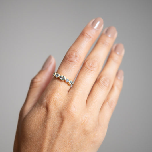 Hand wearing a ring with five stones on a neutral background