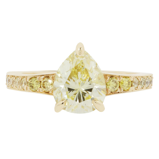 Gold ring with a large pear-shaped yellow diamond and smaller diamonds on the band against a white background