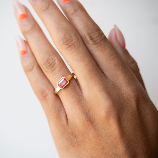 Hand wearing a gold ring with a pink gemstone on a white background