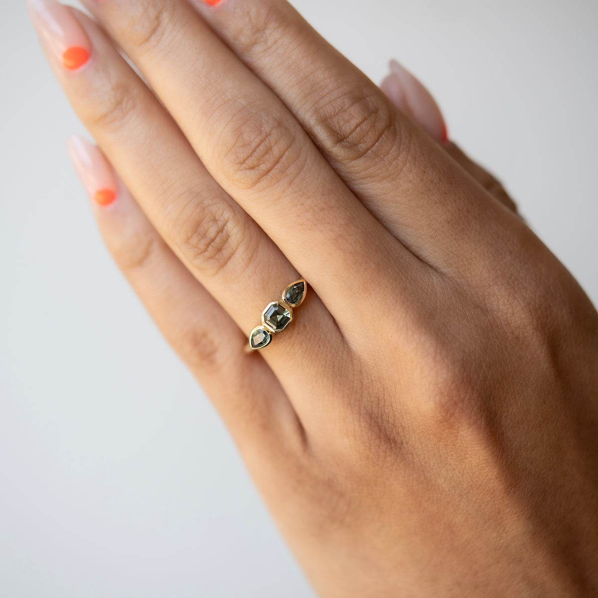 Hand wearing a gold ring with gemstones on a plain background