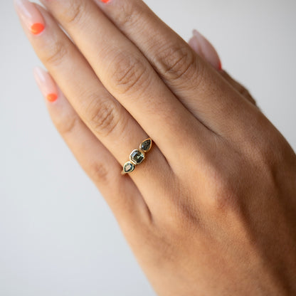Hand wearing a gold ring with gemstones on a plain background