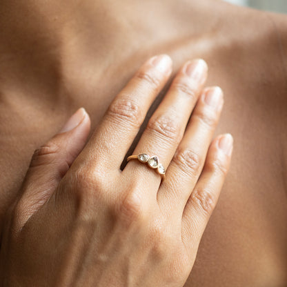 A close-up of a person's hand resting on their chest, wearing a delicate gold ring with two small clear pear-shaped stones.