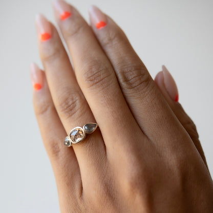 Hand wearing a ring with a visible gemstone on a plain background