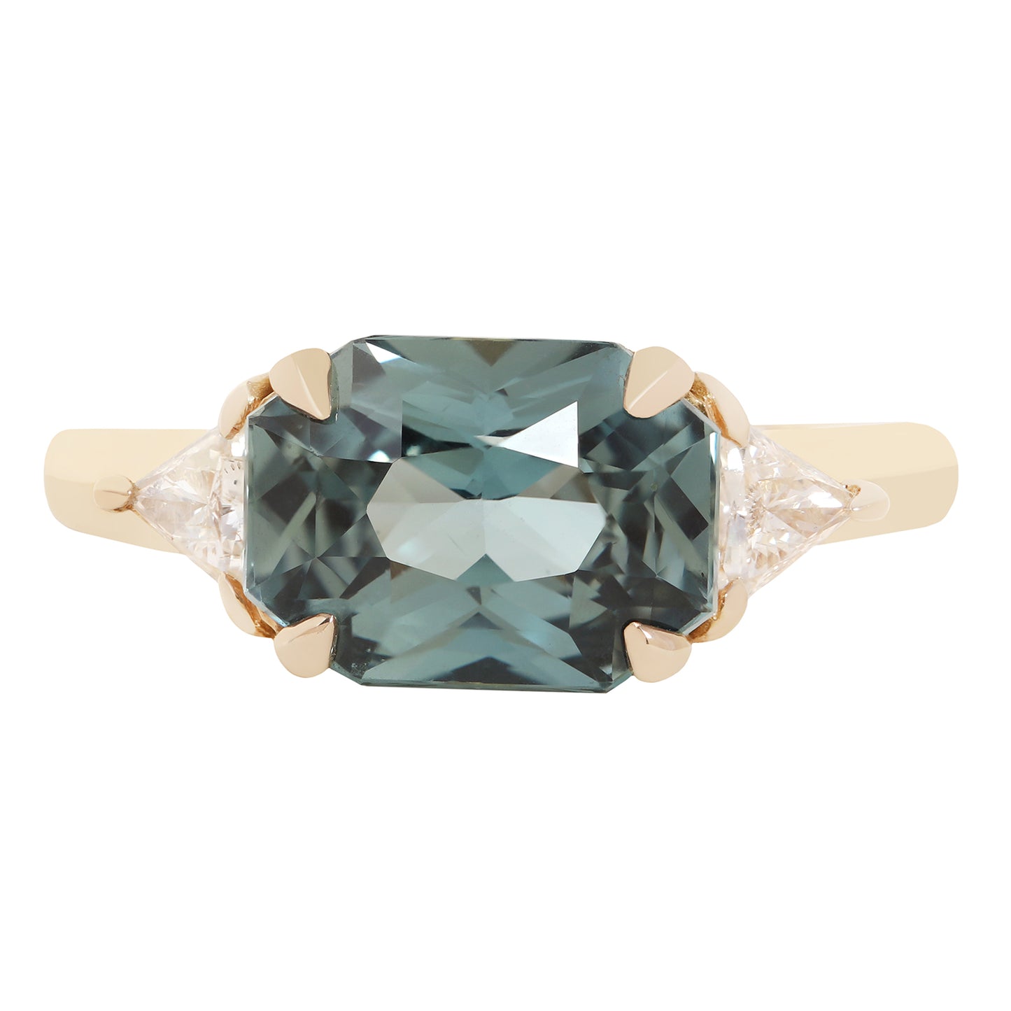 An emerald-cut blue sapphire ring set in a yellow gold four-prong setting with small round and marquise-cut side diamonds, shown against a plain white background.