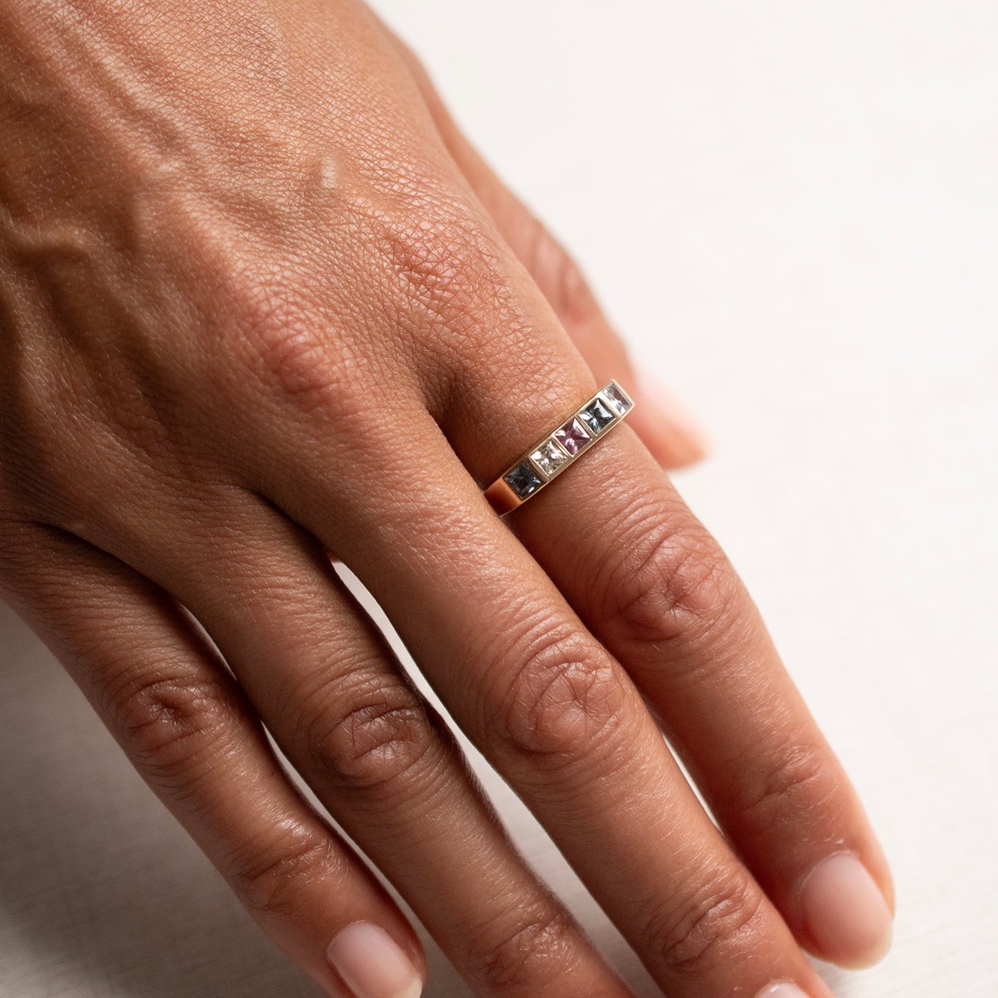 A close-up of a person's hand wearing a slim silver band ring with a row of small clear stones on a plain light background.