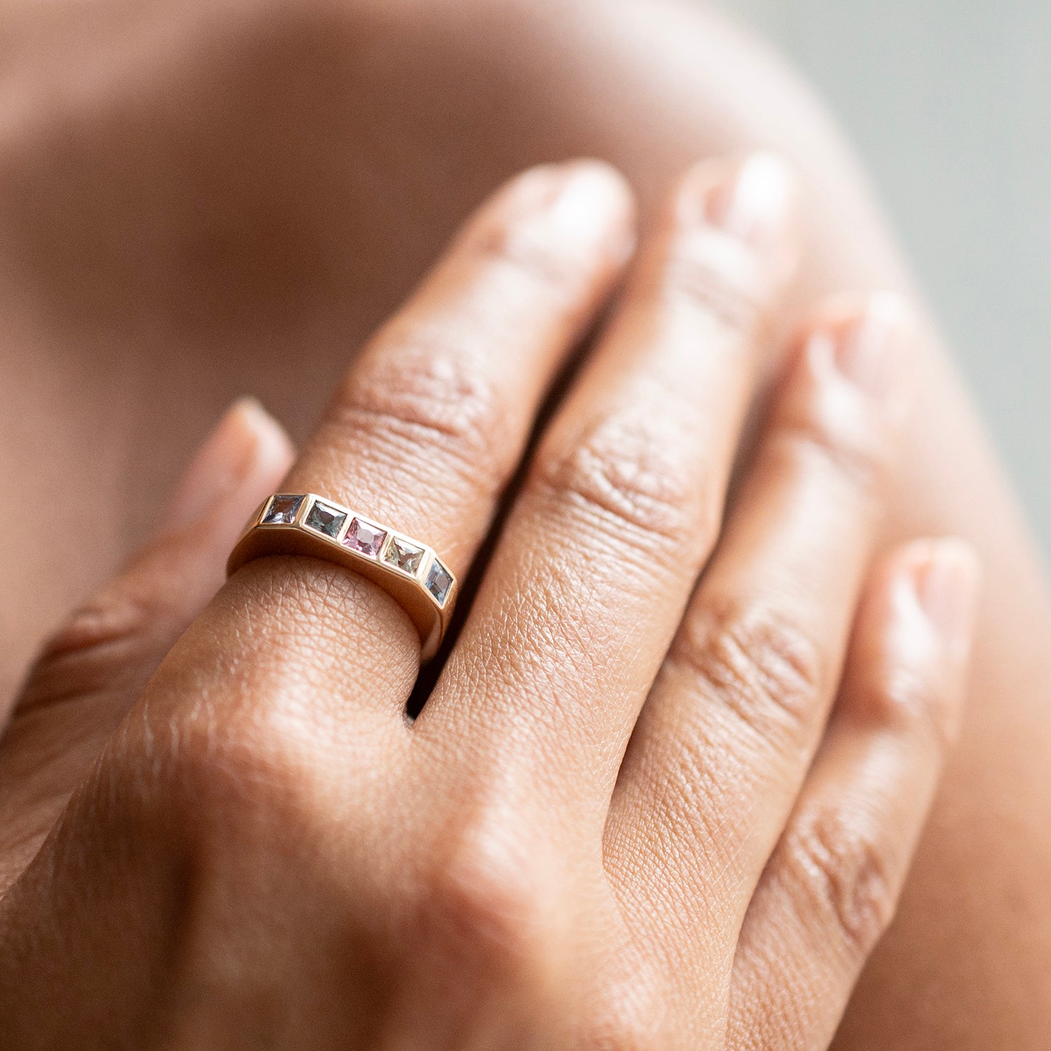A close-up of a hand wearing a rose gold band ring with a row of small square pink gemstones.