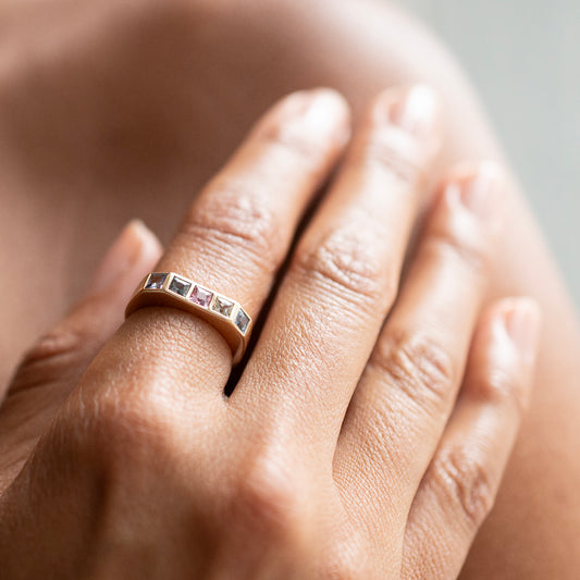 A close-up of a hand wearing a rose gold band ring with a row of small square pink gemstones.