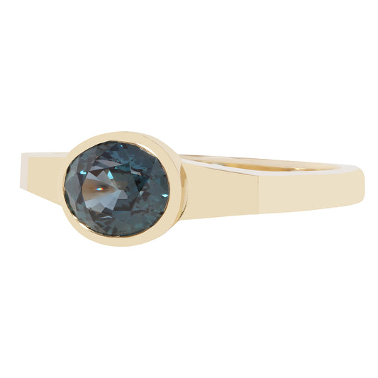 A yellow gold ring featuring a bezel-set oval faceted dark blue gemstone, shown against a plain white background.