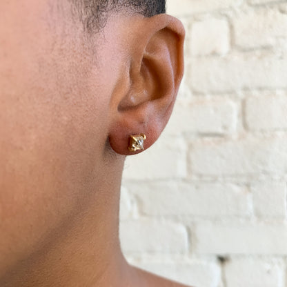 Lauren Wolf - Close-up of an ear wearing a gold earring with a diamond on a light stone wall background