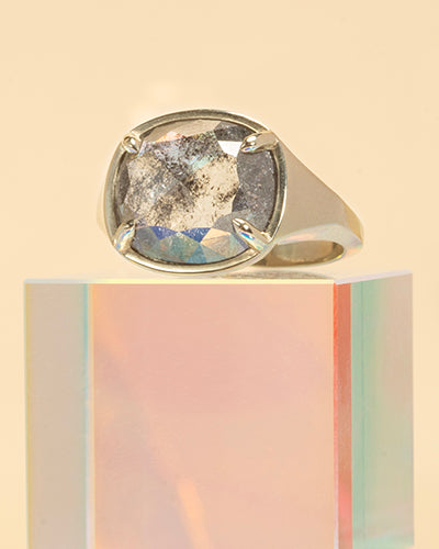 Gold ring with a large, round, faceted diamond on a light beige background