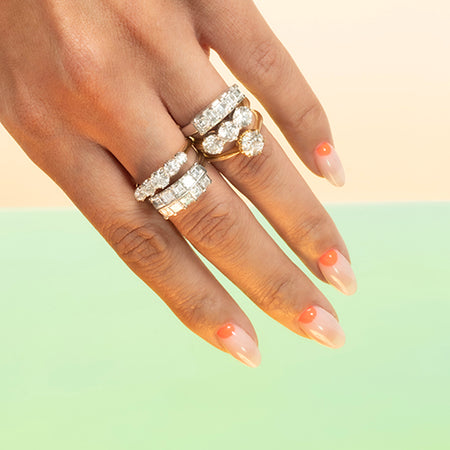 Hand wearing multiple diamond rings on a light green background