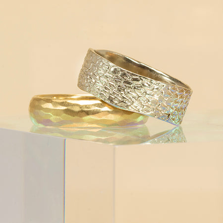 Two gold rings with textured surfaces on a reflective surface.