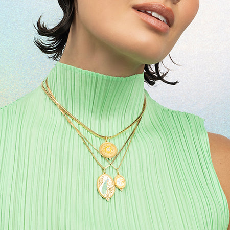 Woman wearing layered gold necklaces with pendants against a light background