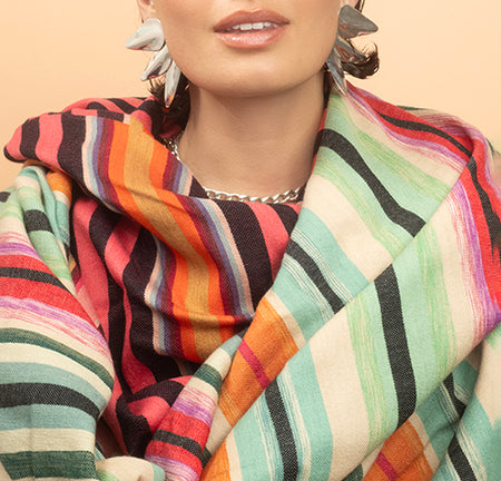 Colorful striped scarfs draped around a person with a neutral background