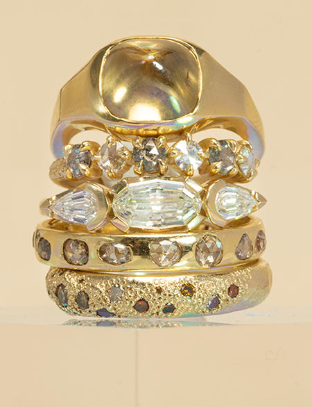 Set of five gold rings with diamond accents on a beige background