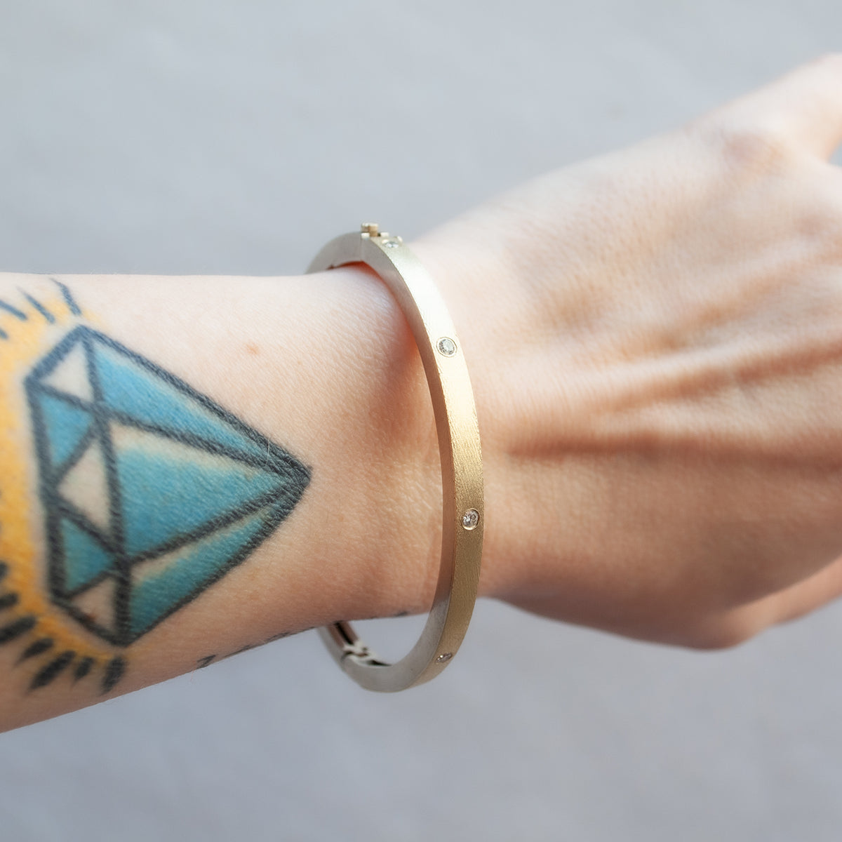 Rene Escobar - Gold bracelet on a wrist with a tattoo of a diamond design.