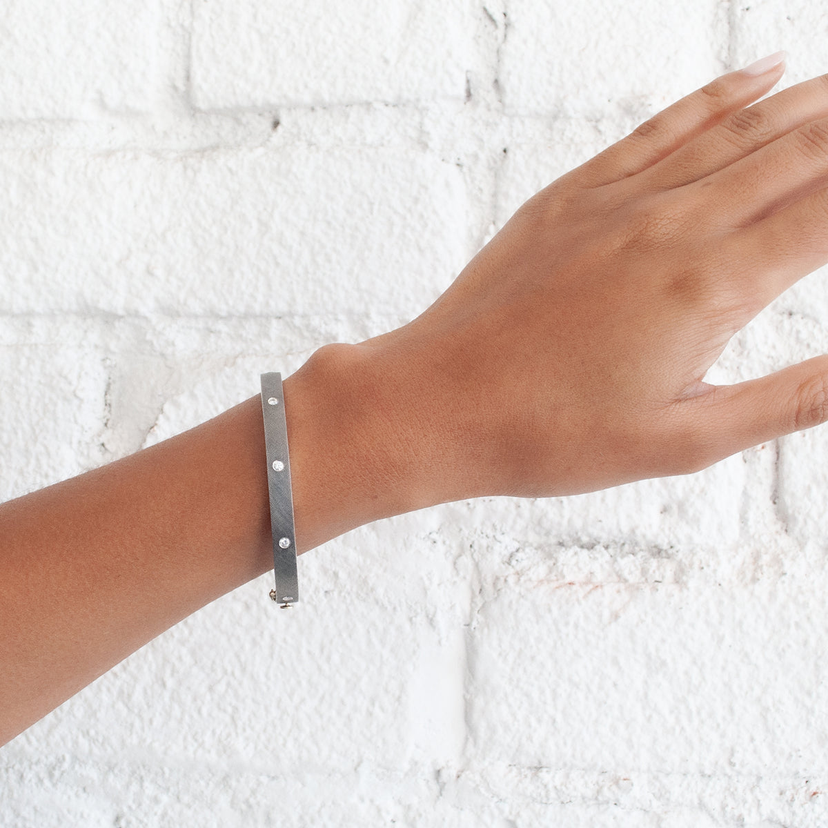 Rene Escobar - Silver bracelet on a wrist against a white textured background