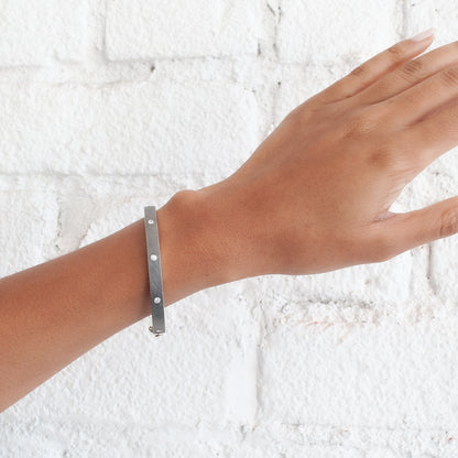 Rene Escobar - Silver bracelet on a wrist against a white textured background