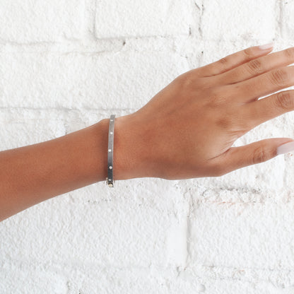 Rene Escobar - Hand wearing a silver bracelet on a textured white background