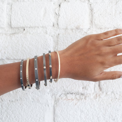 Rene Escobar - Hand wearing multiple silver  and gold bracelets on a textured white background