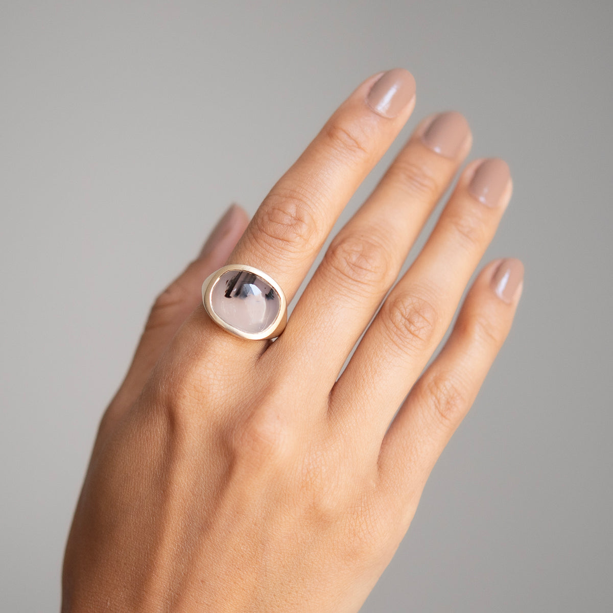 Hand wearing a ring with a gray stone on a neutral background