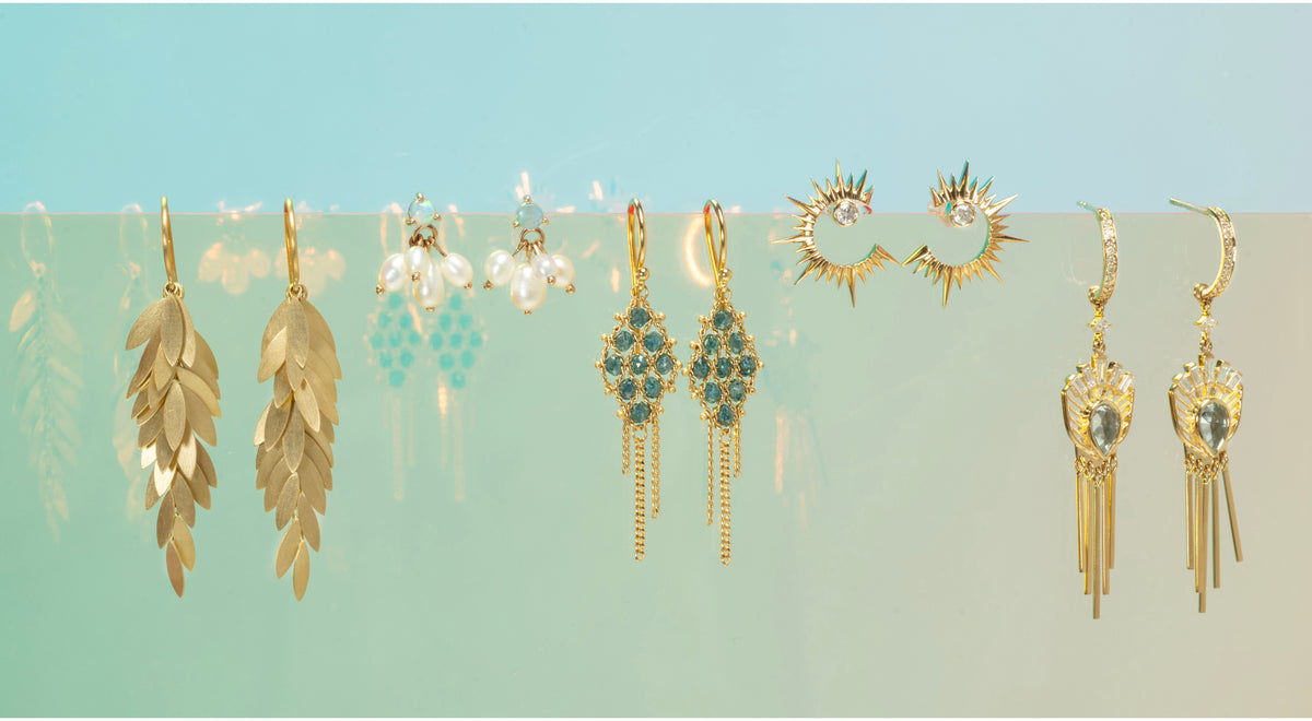 Collection of gold earrings on a light blue and green gradient background