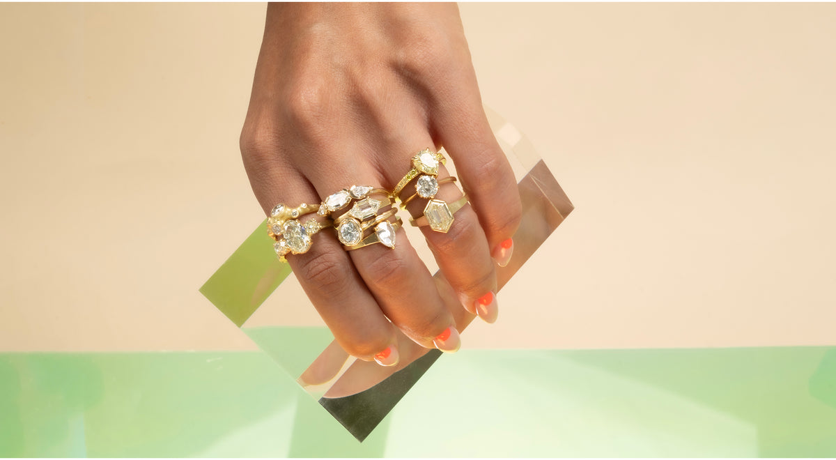 Hand wearing multiple gold rings with gemstones on a gradient background