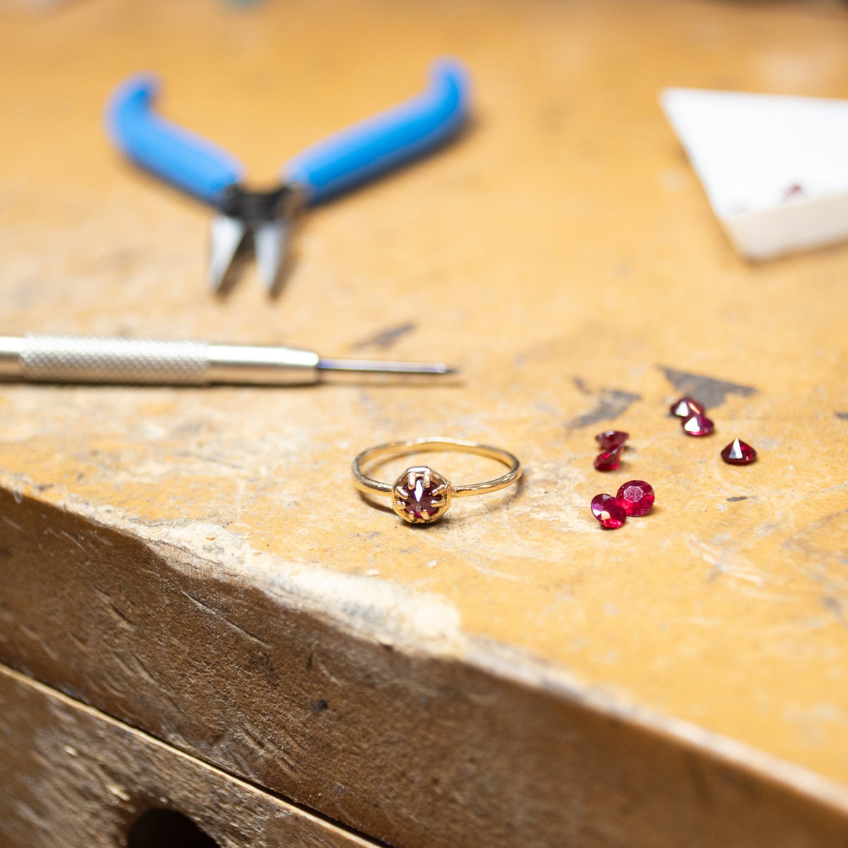 Jewelry-making process on a workbench with tools and gemstones.