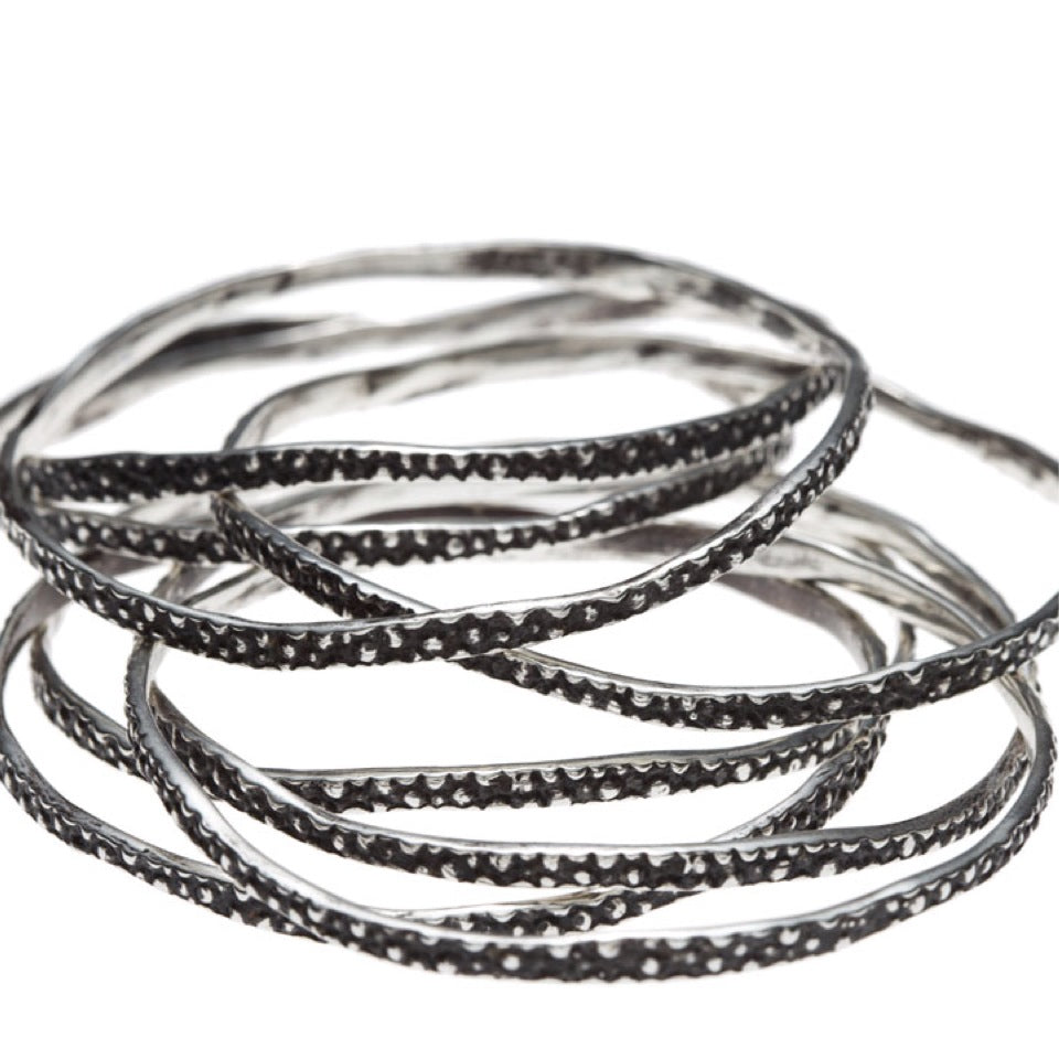 A stack of Silver Stingray Bangles by Lauren Wolf Jewelry shown on a white background